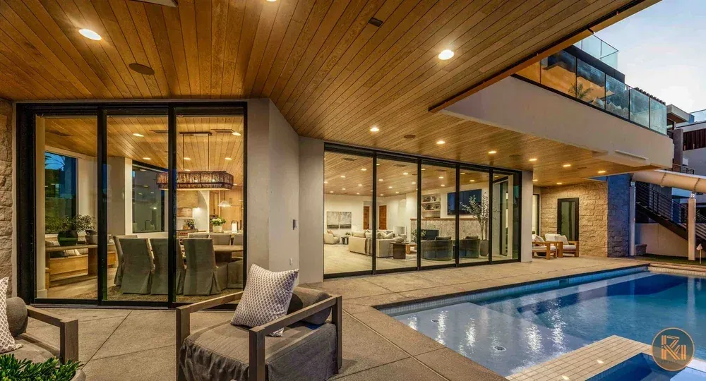 Modern home with illuminated glass walls, covered patio and swimming pool at dusk, photographed by Sam Reed.