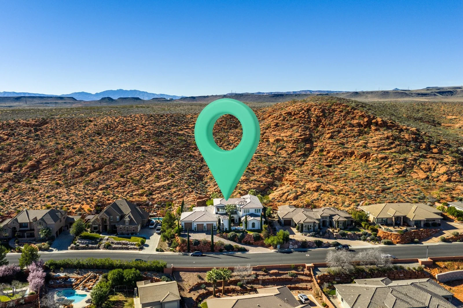 Aerial view of homes below red desert hills, with a mint-green location marker above the central white house