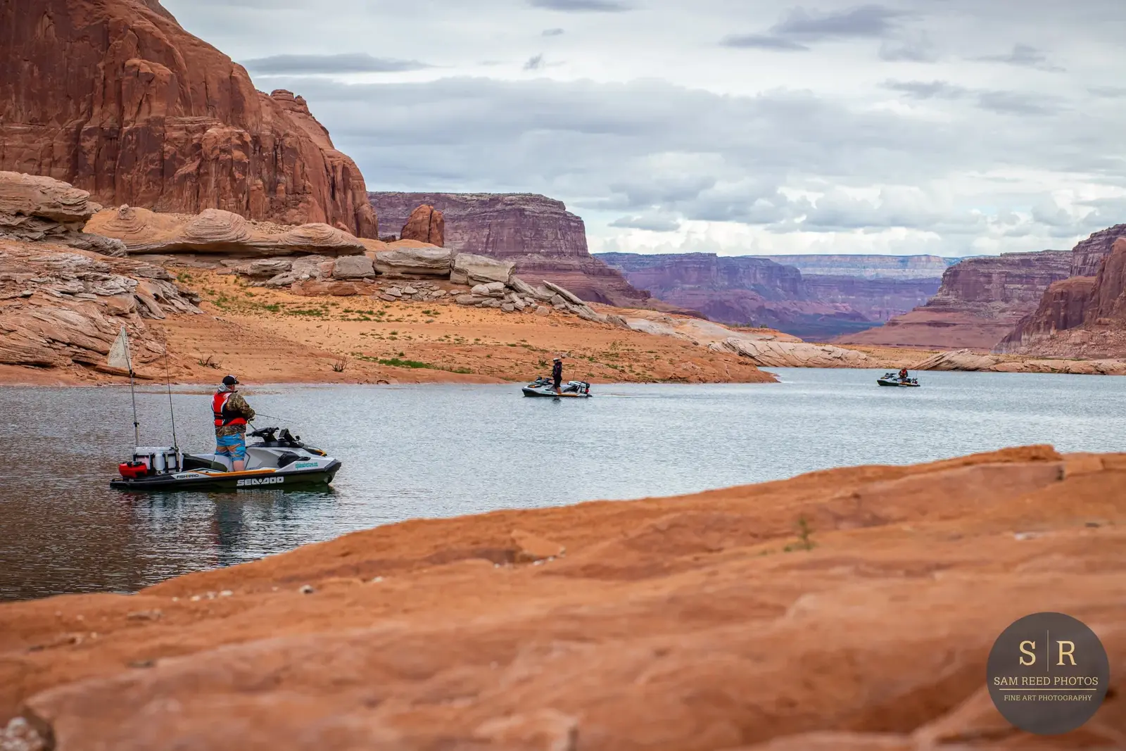 Three people fishing from boats on a lake surrounded by canyon walls with a cloudy sky.