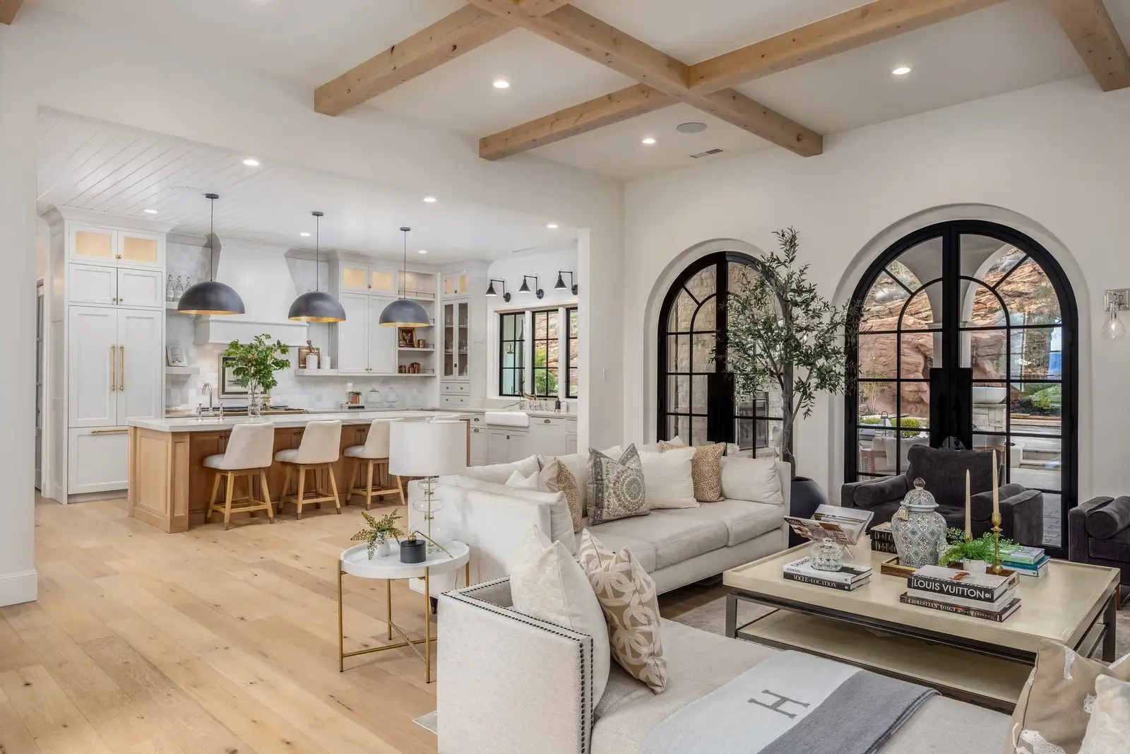 Open-plan living room and kitchen with exposed wood beams and arched glass doors at the Sunset property