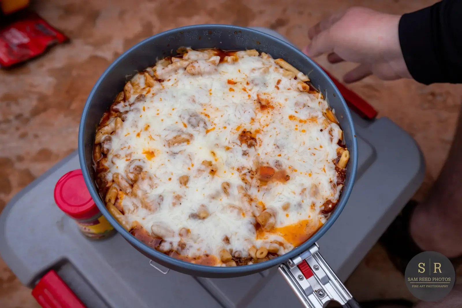A pan of baked ziti with melted cheese, pasta, and tomato sauce, sitting on a small table.