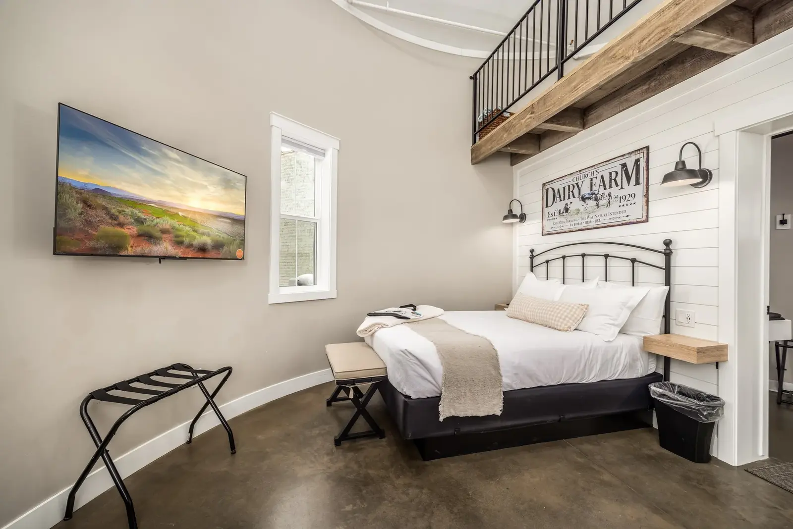 Rustic bedroom beneath a loft railing at The Silo Suites