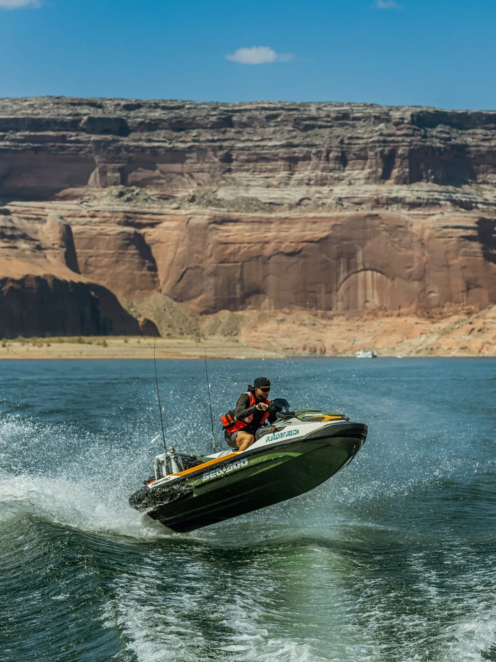 A man riding a speedboat on a lake with rocky cliffs in the background under a clear blue sky.