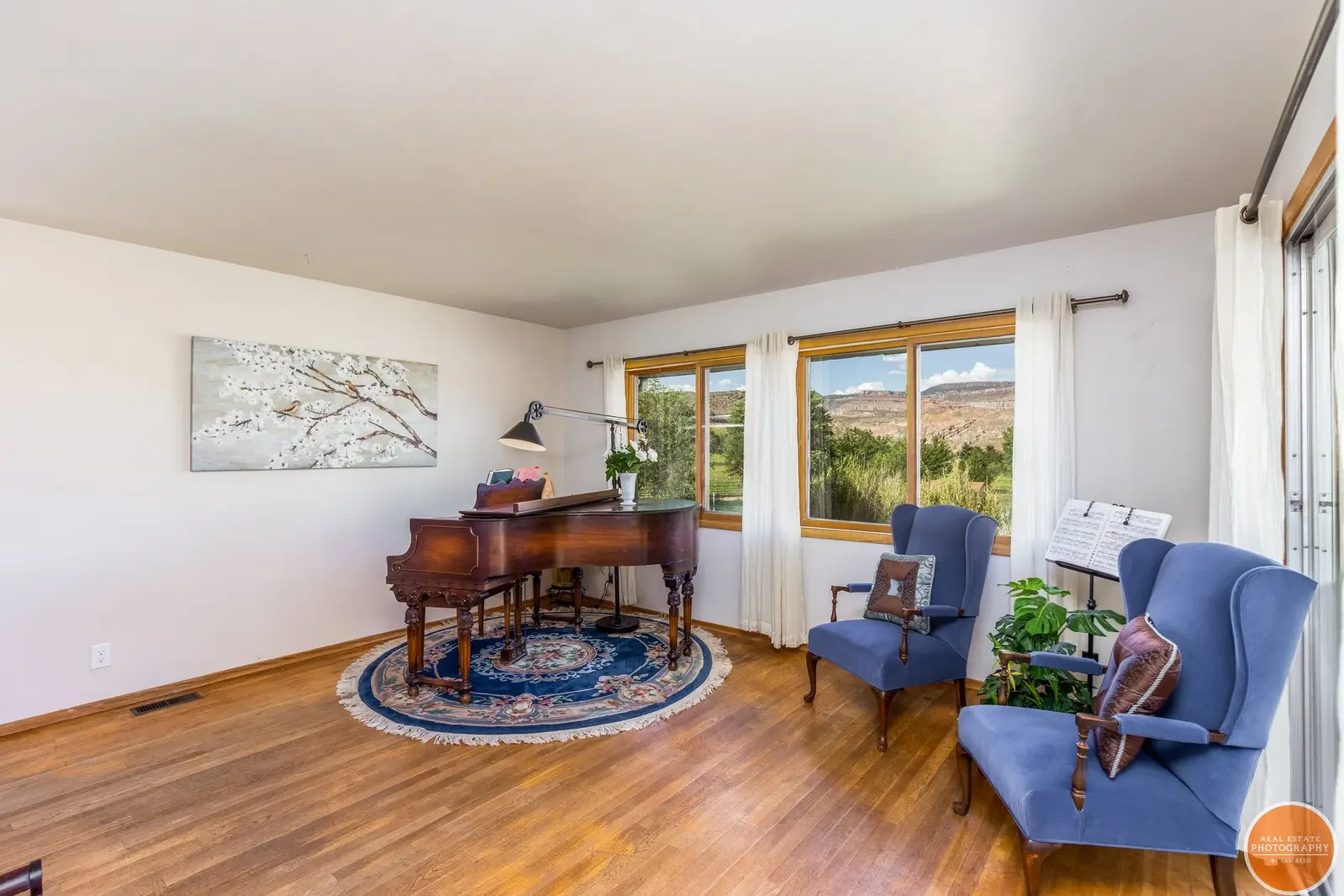 Living room with a piano, two blue armchairs, and large windows.