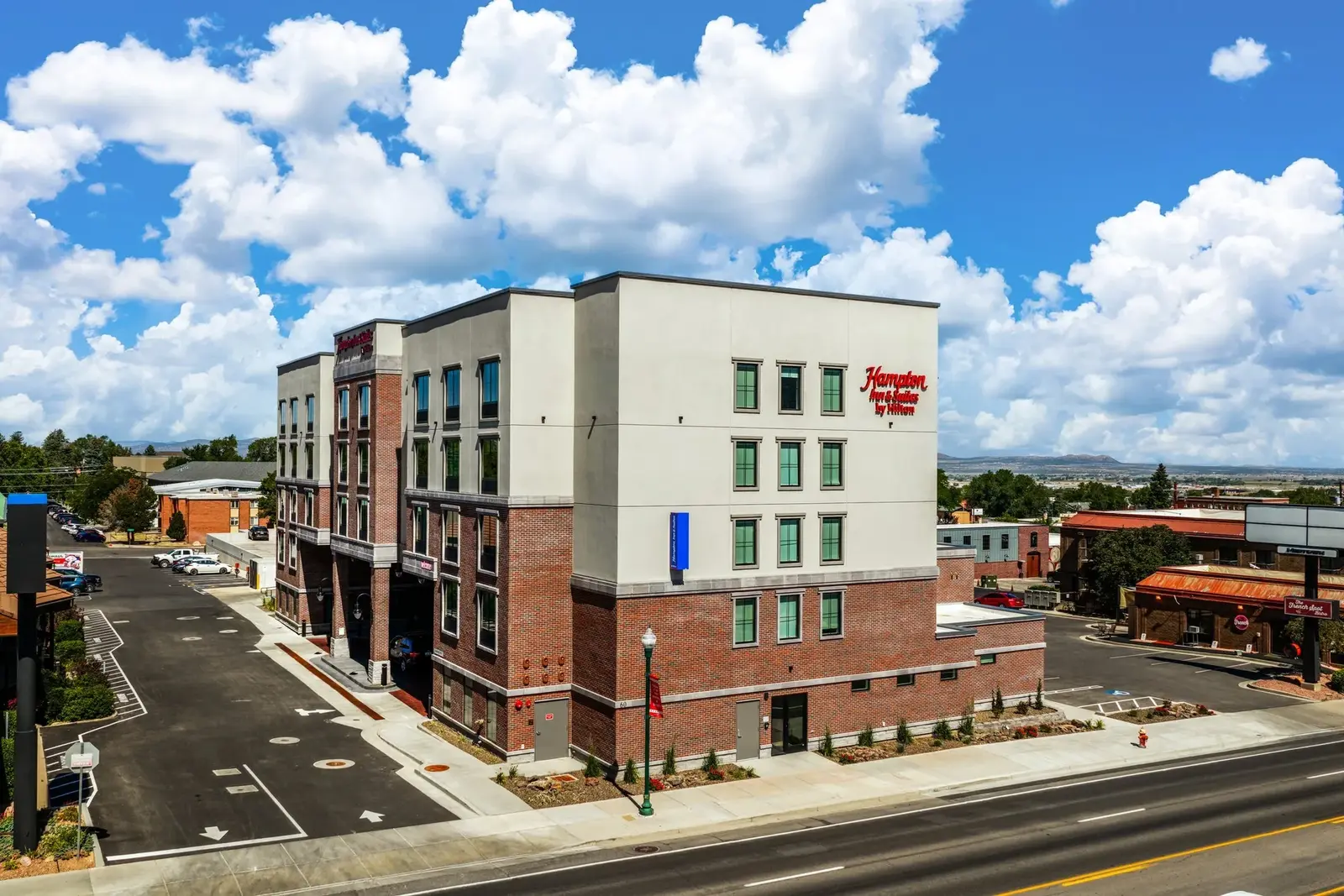Hampton Inn & Suites in Cedar City, photographed from an elevated corner view beneath bright clouds.