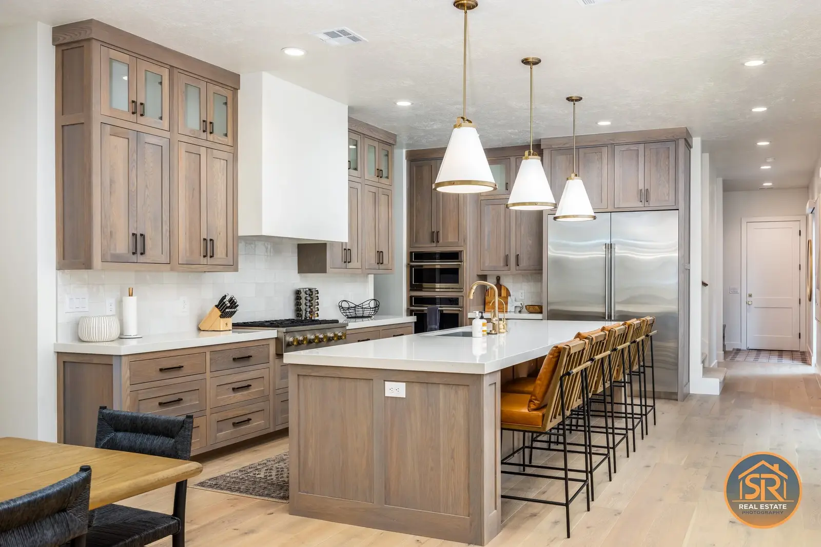 Kitchen with tall wood cabinets and a long island beneath white pendant lights — from Sam Reed’s photography portfolio