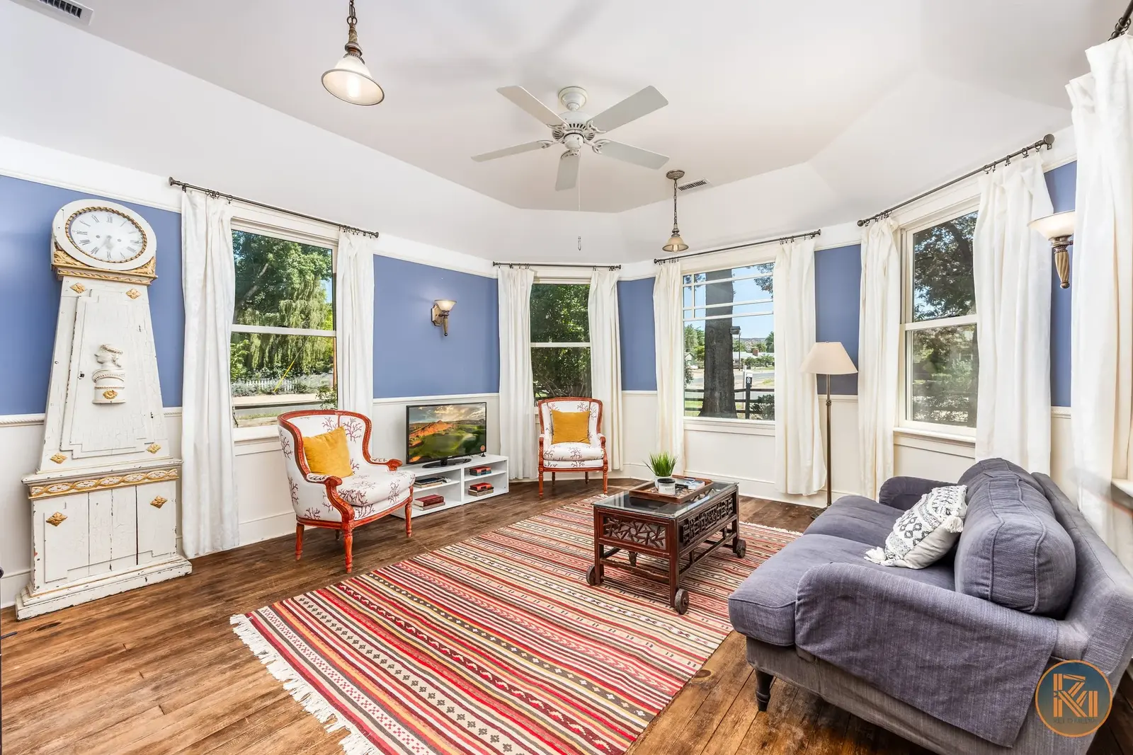 Bright sitting room with blue walls, tall windows, and a striped rug.