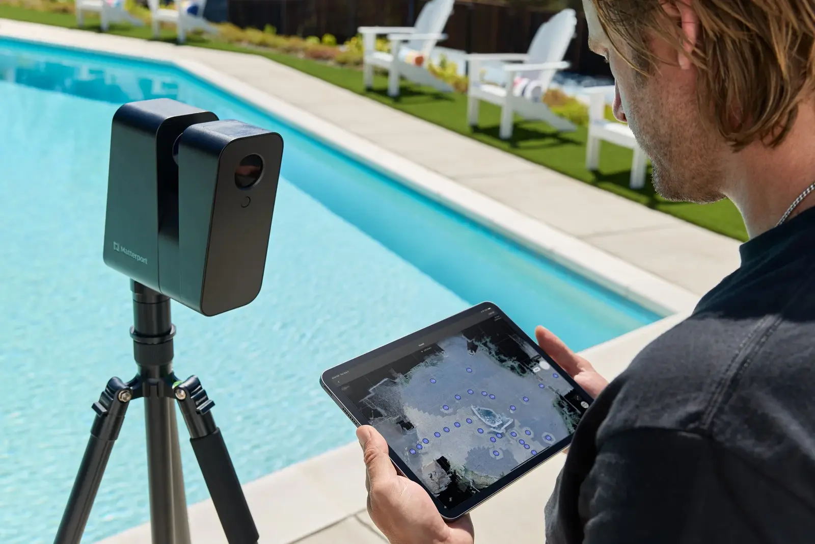 A man assessing a property from a tablet device using drone mapping technology by a swimming pool in a backyard.