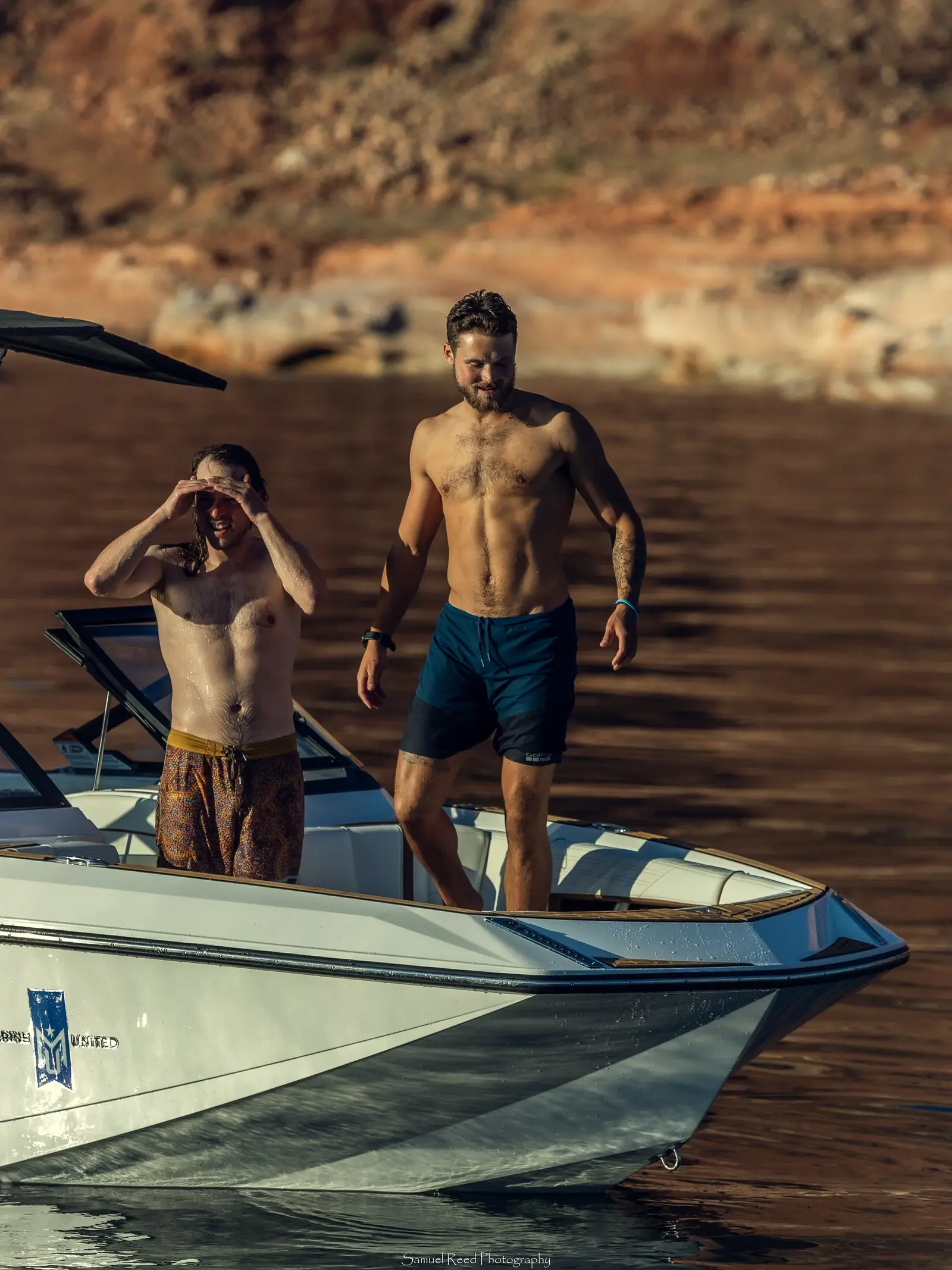 Two men on a boat in a lake or river, with rocky cliffs in the background, enjoying a sunny day.