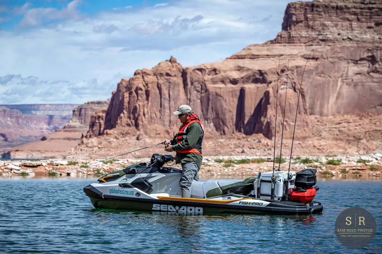 A person fishing from a jet ski on a lake with red rock formations in the background.