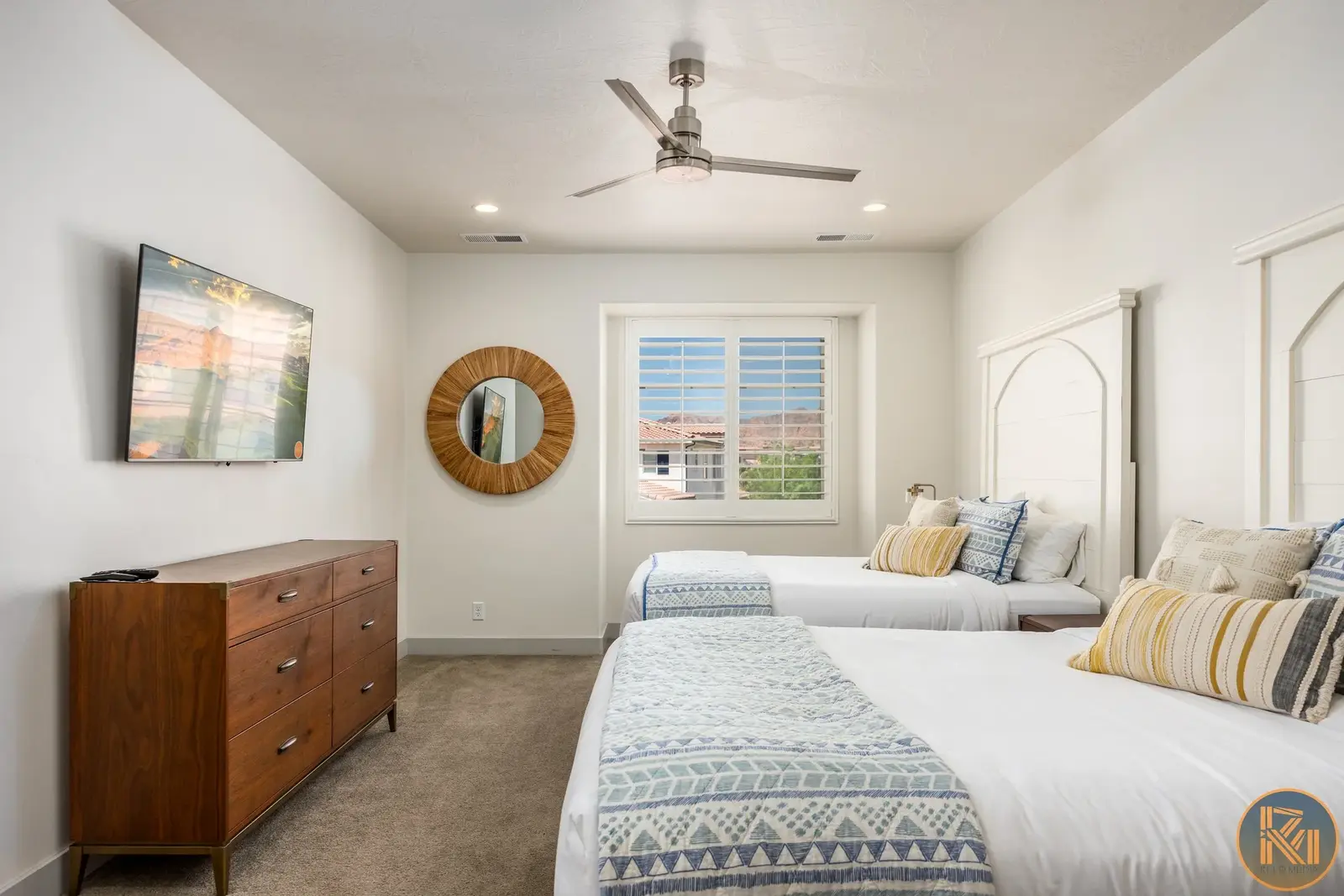Bright bedroom with two beds, a wooden dresser, and a ceiling fan.