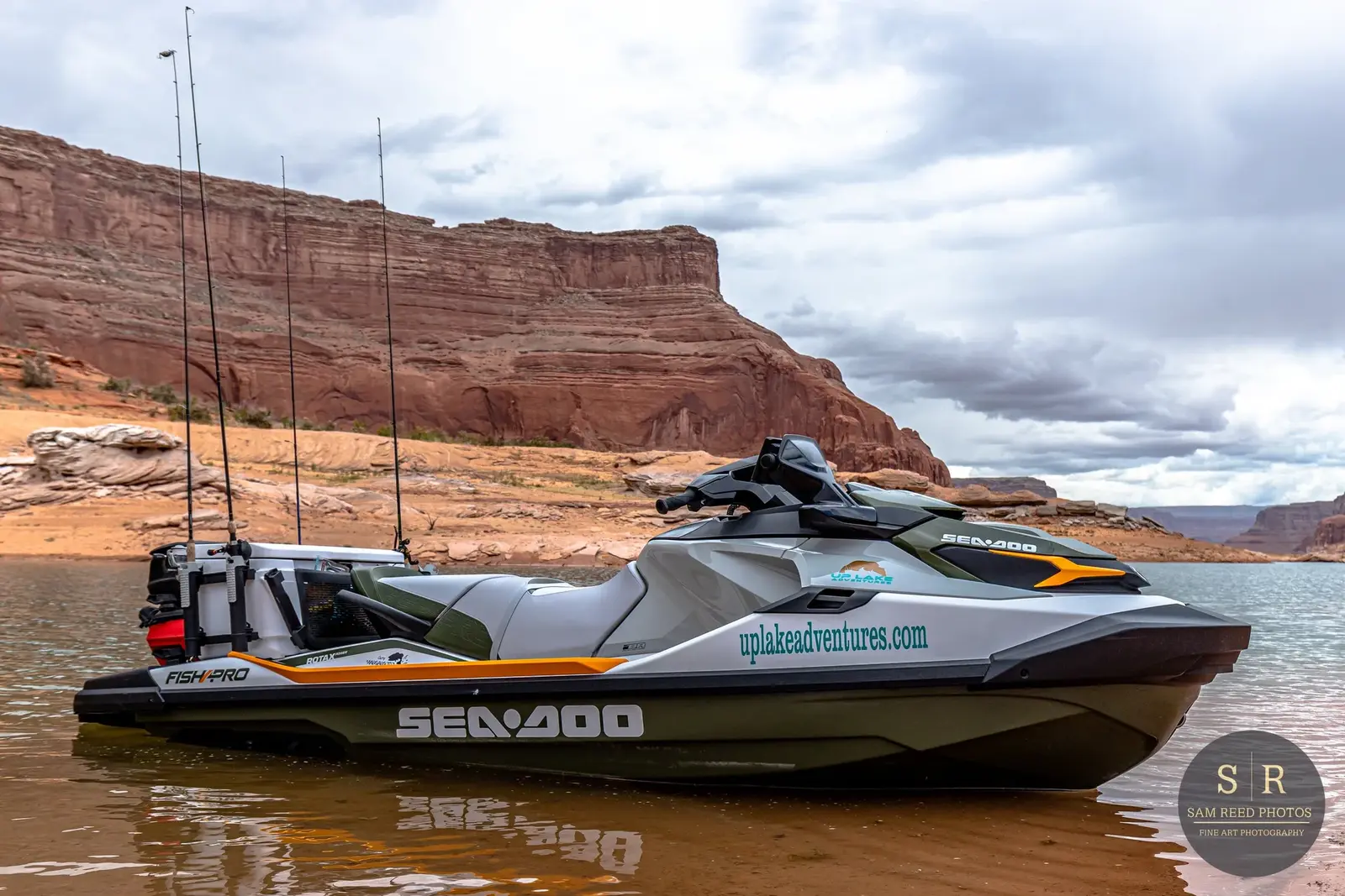 A sleek Sea-Doo personal watercraft floating on calm water with red rock canyon walls and cloudy sky in the background.