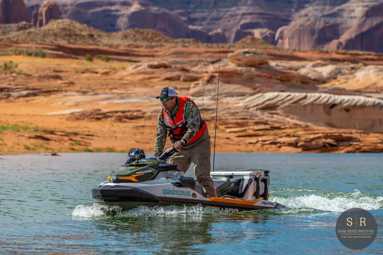 Man riding a jet ski on a lake with red rock formations in the background.