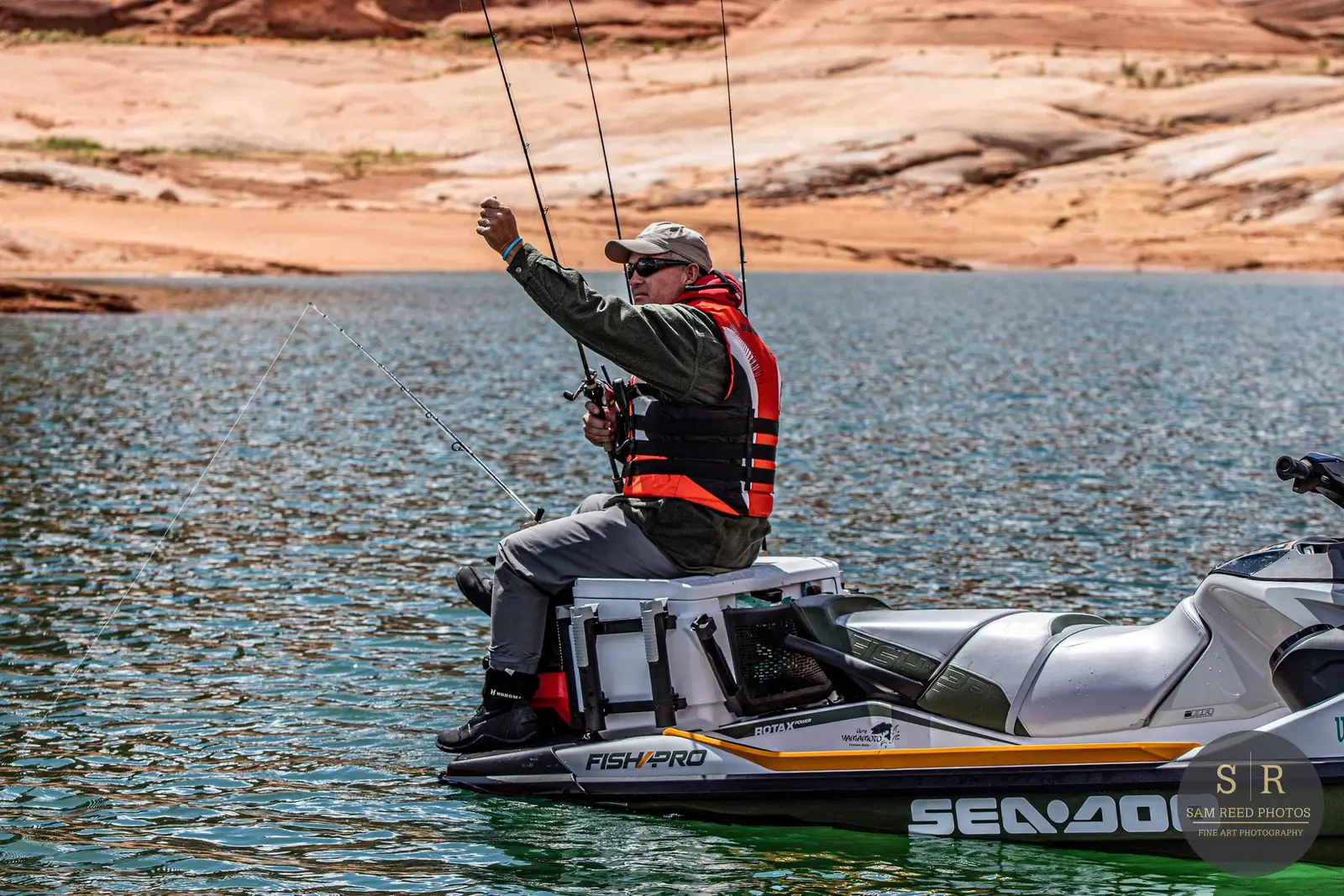 A man fishing from a boat on a lake with a desert landscape in the background.