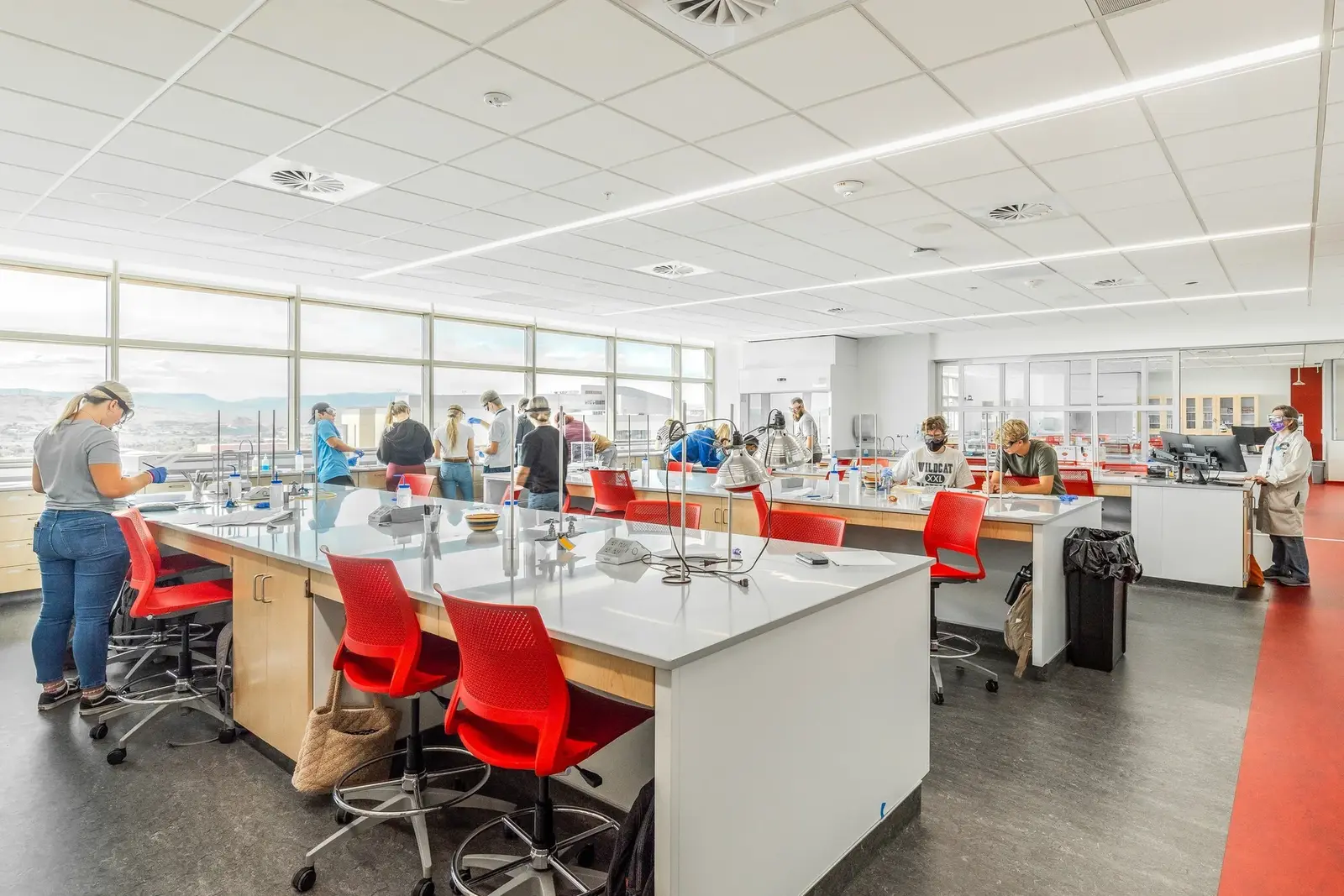 Bright laboratory interior with white workbenches, red chairs and occupants at work.