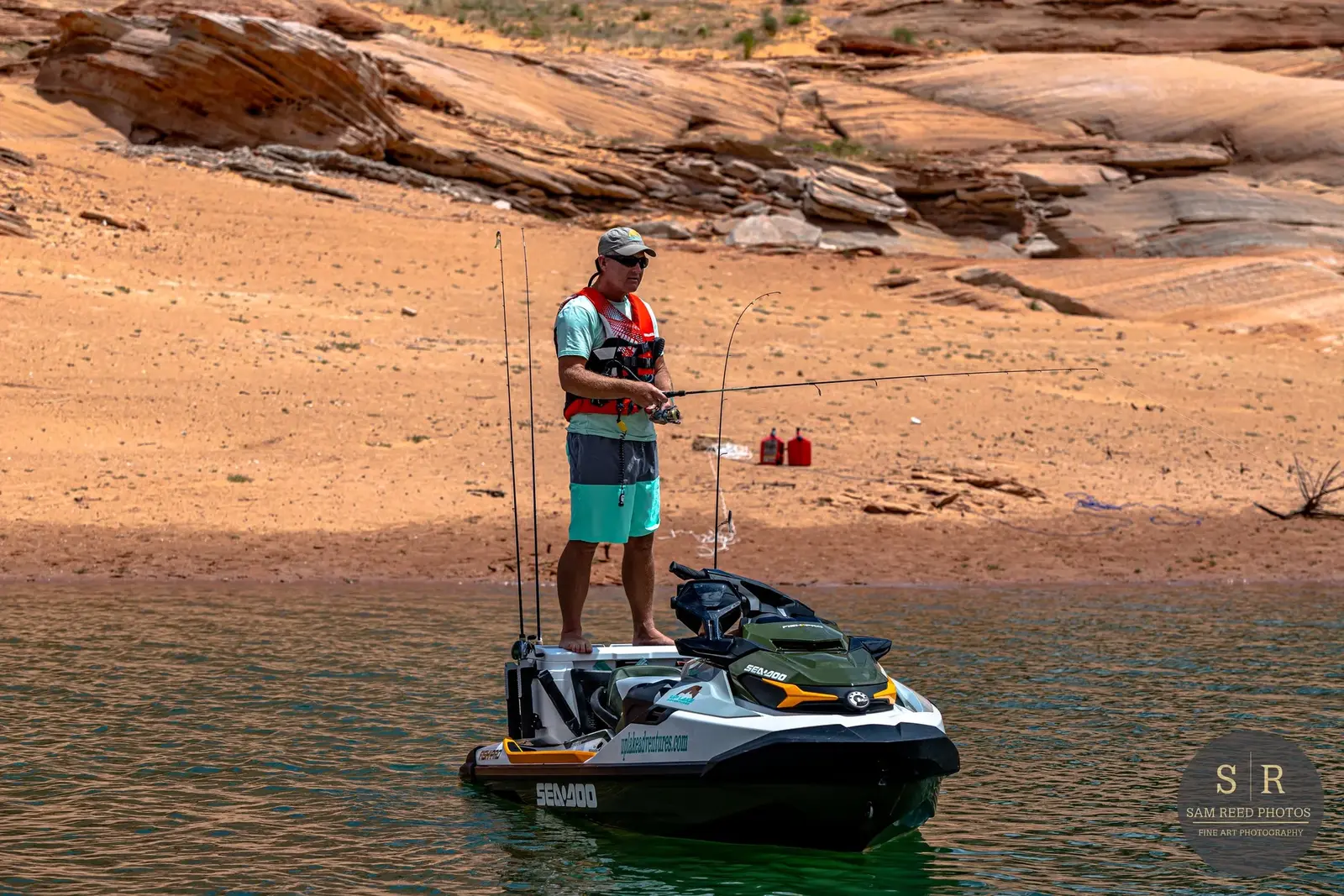 A man fishing from a kayak on a body of water with a desert landscape and rocky hills in the background.