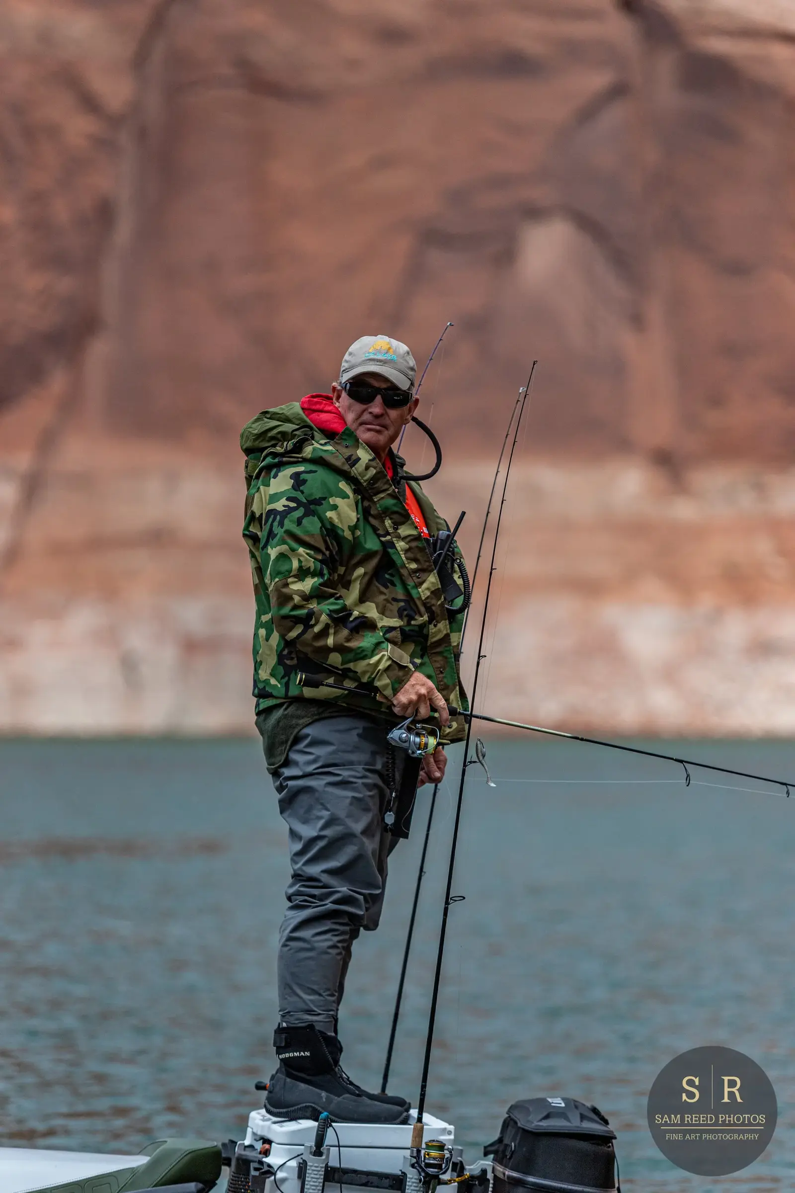 Man fishing on a boat in a lake, with red rock formations in the background.