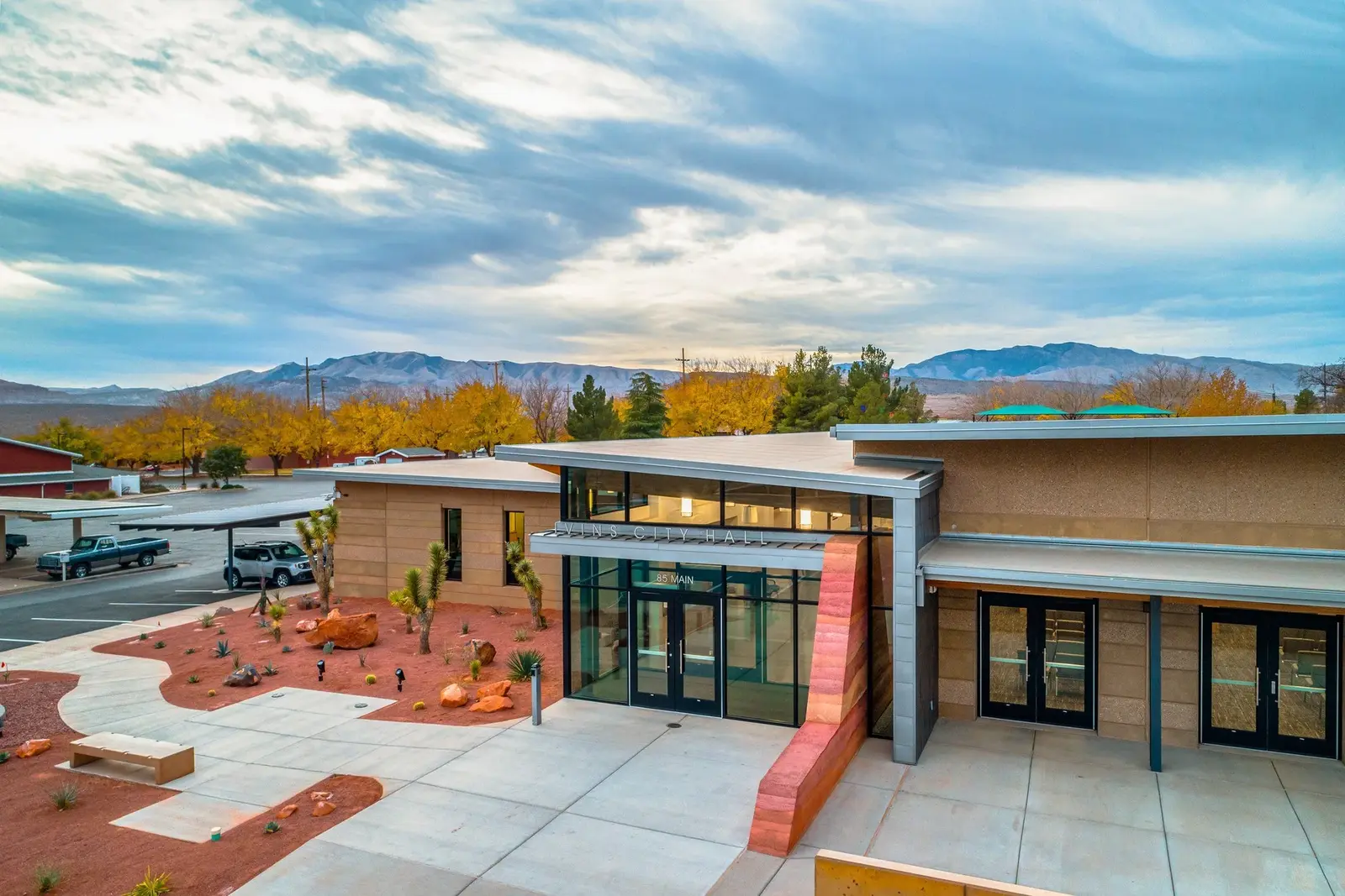 Elevated view of the glass entrance and plaza beneath a textured evening sky.