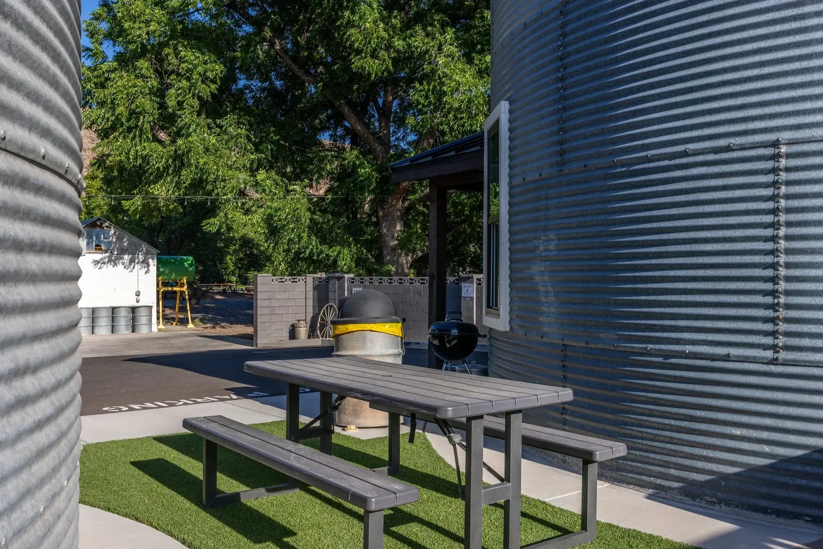 Outdoor picnic table and grill beside a curved metal silo at The Silo Suites
