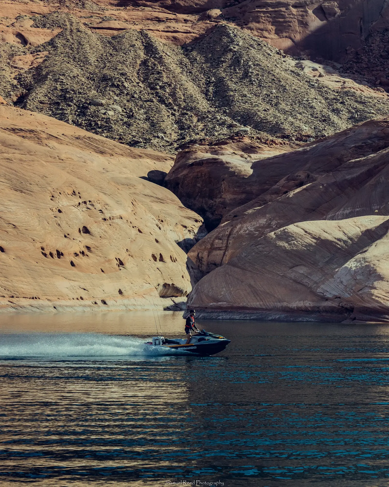 A person riding a motorboat on a calm body of water surrounded by large rocky canyon walls.