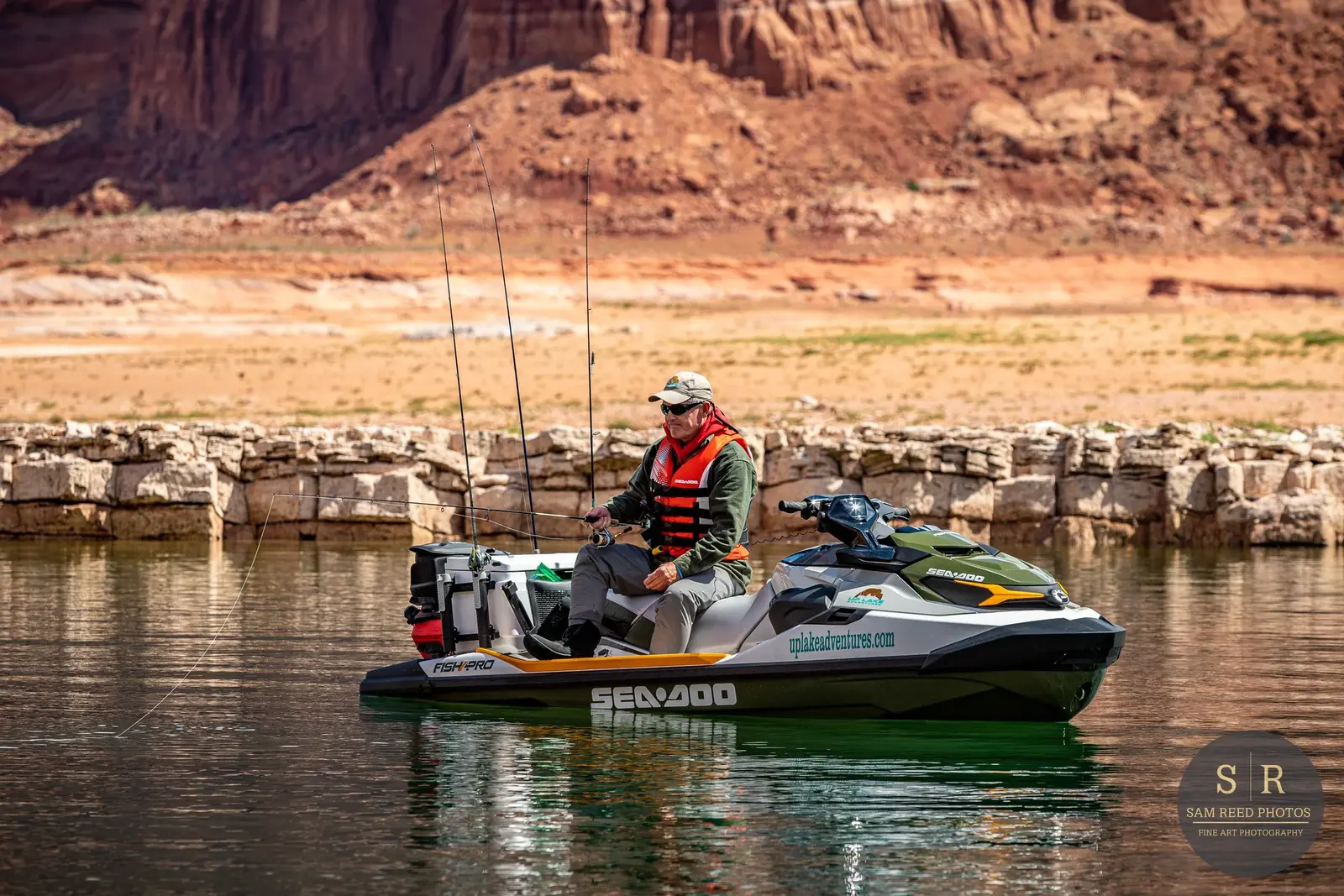 A man fishing on a jet ski in a calm body of water with rocky and mountainous terrain in the background.