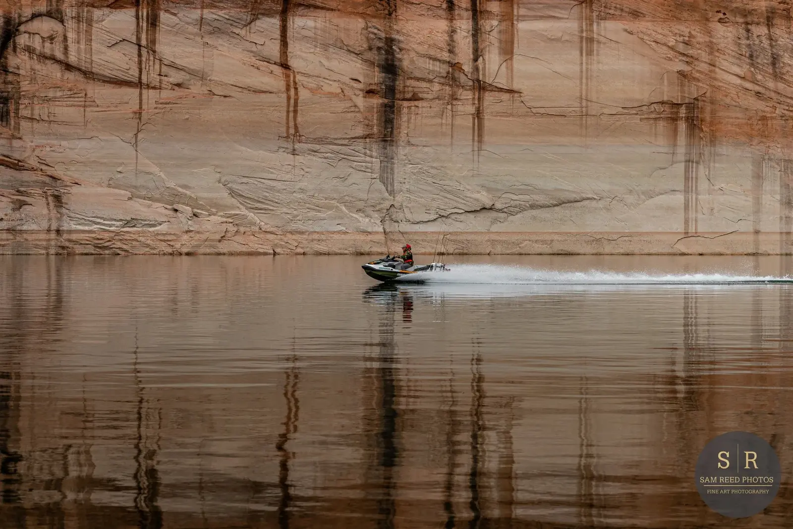 A person riding a jet ski on calm water with a large rocky cliff in the background.