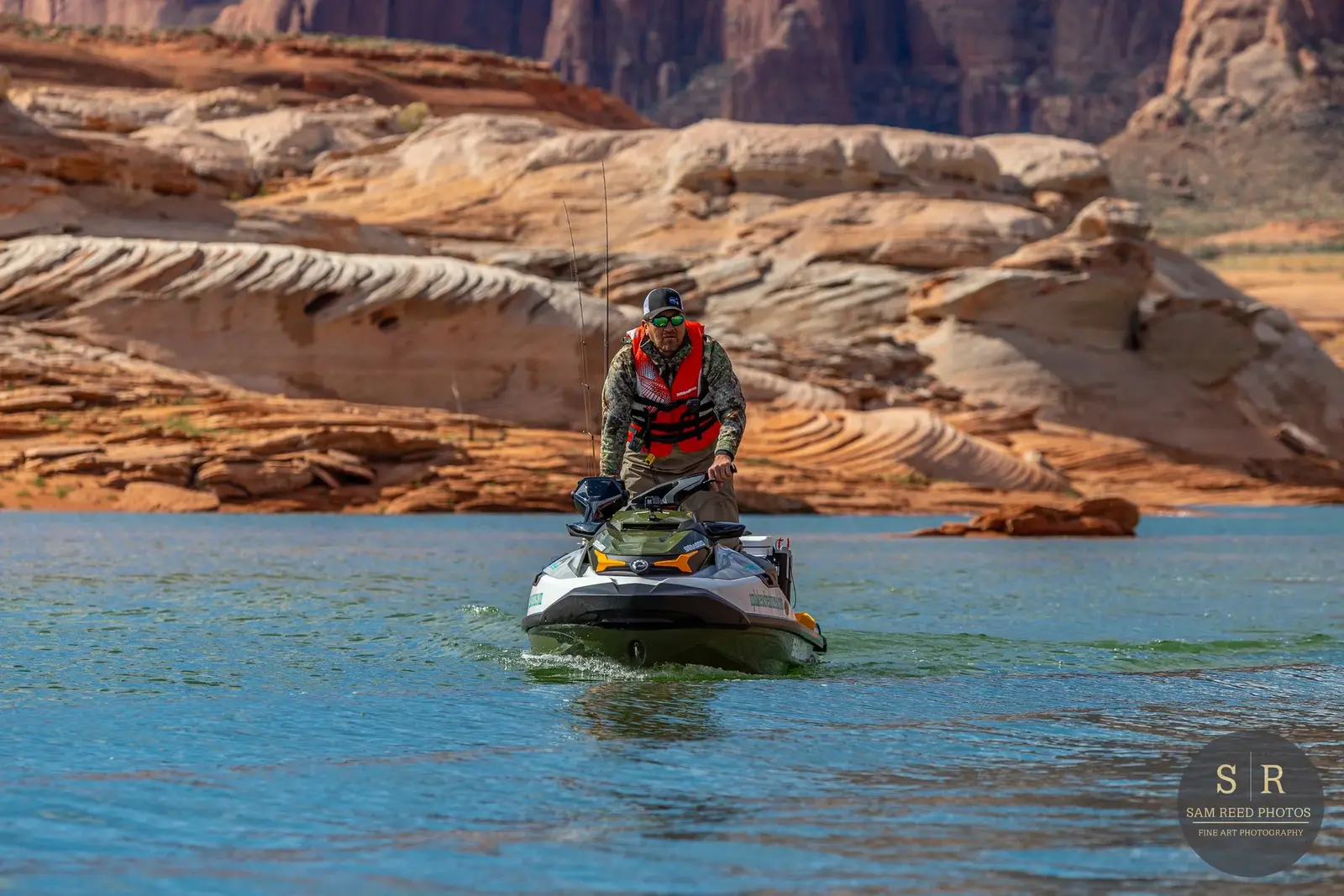 A man operating a personal watercraft or jet ski on a body of water, with rocky canyon landscape in the background.