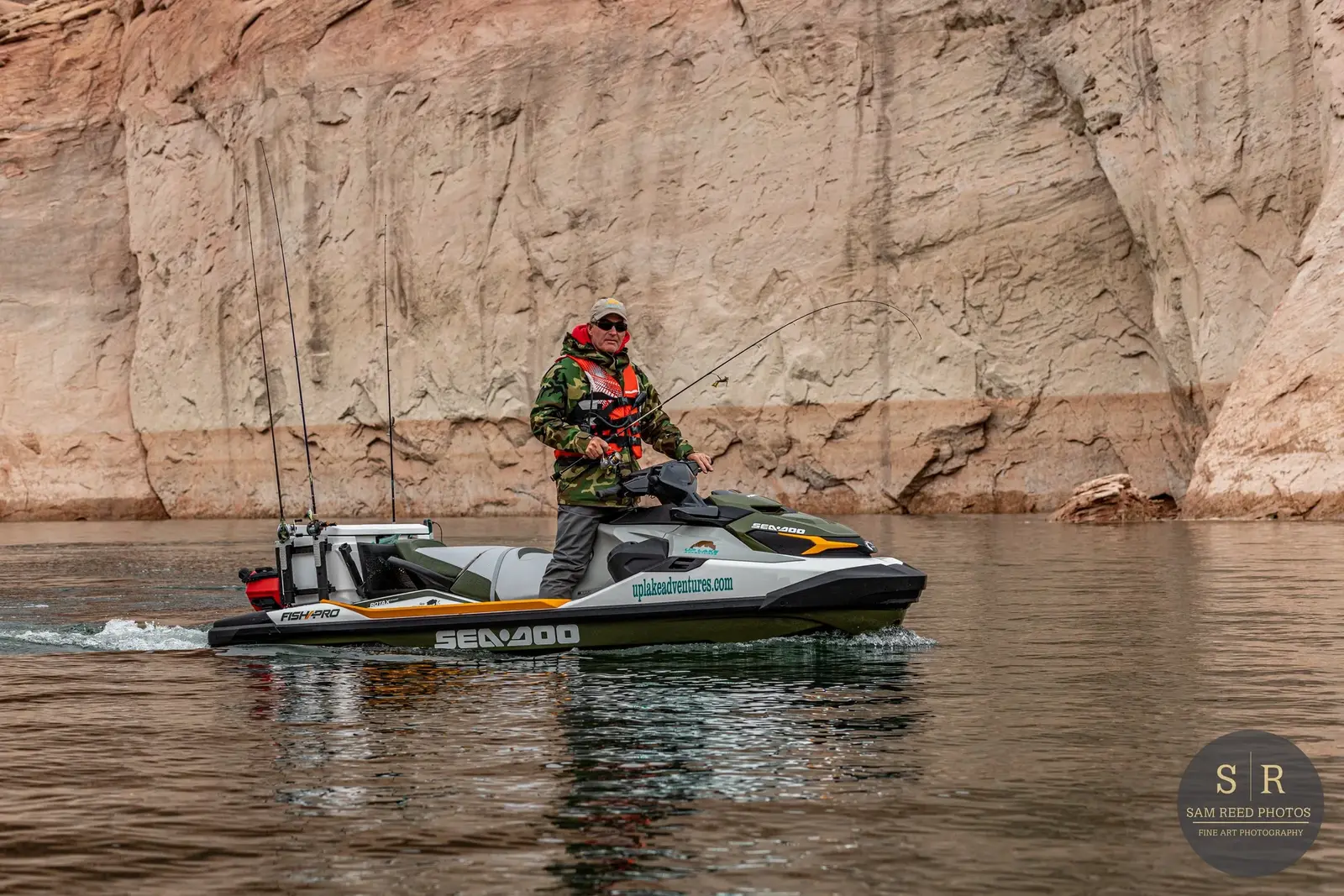 Man fishing on a Sea-Doo watercraft on a calm river with cliffs in the background.