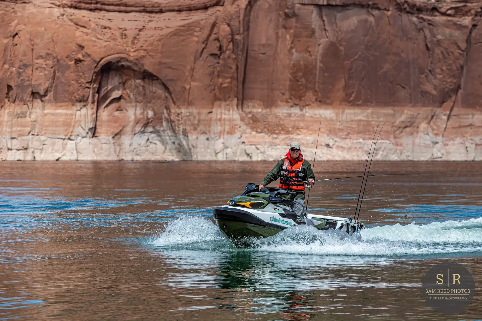 A man riding a jet ski on a body of water with large red rock cliffs in the background.