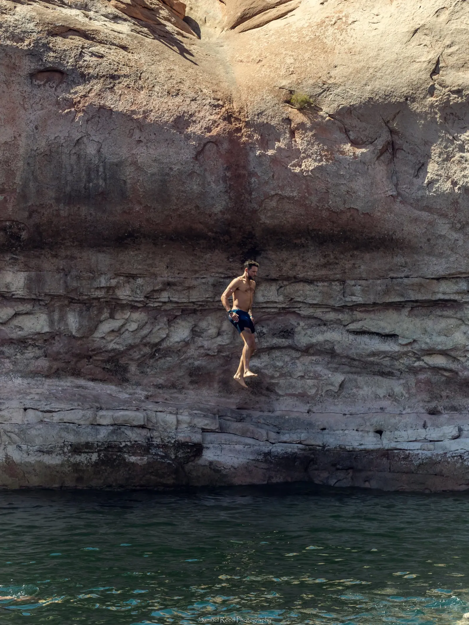 A man in swim trunks jumping off a rocky ledge into water below at a cliffside.