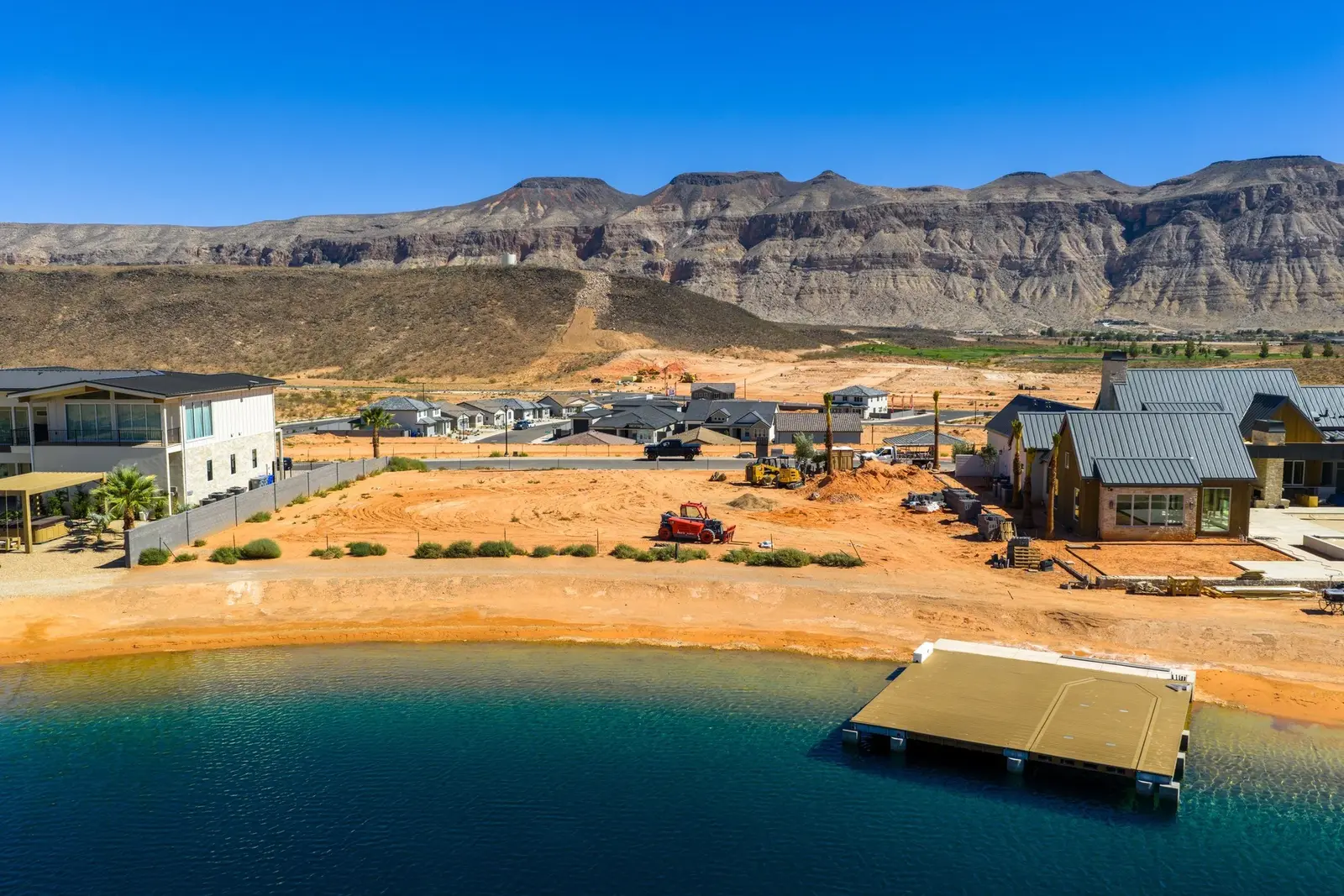 Aerial view across the water toward a sandy open lot between neighboring buildings.