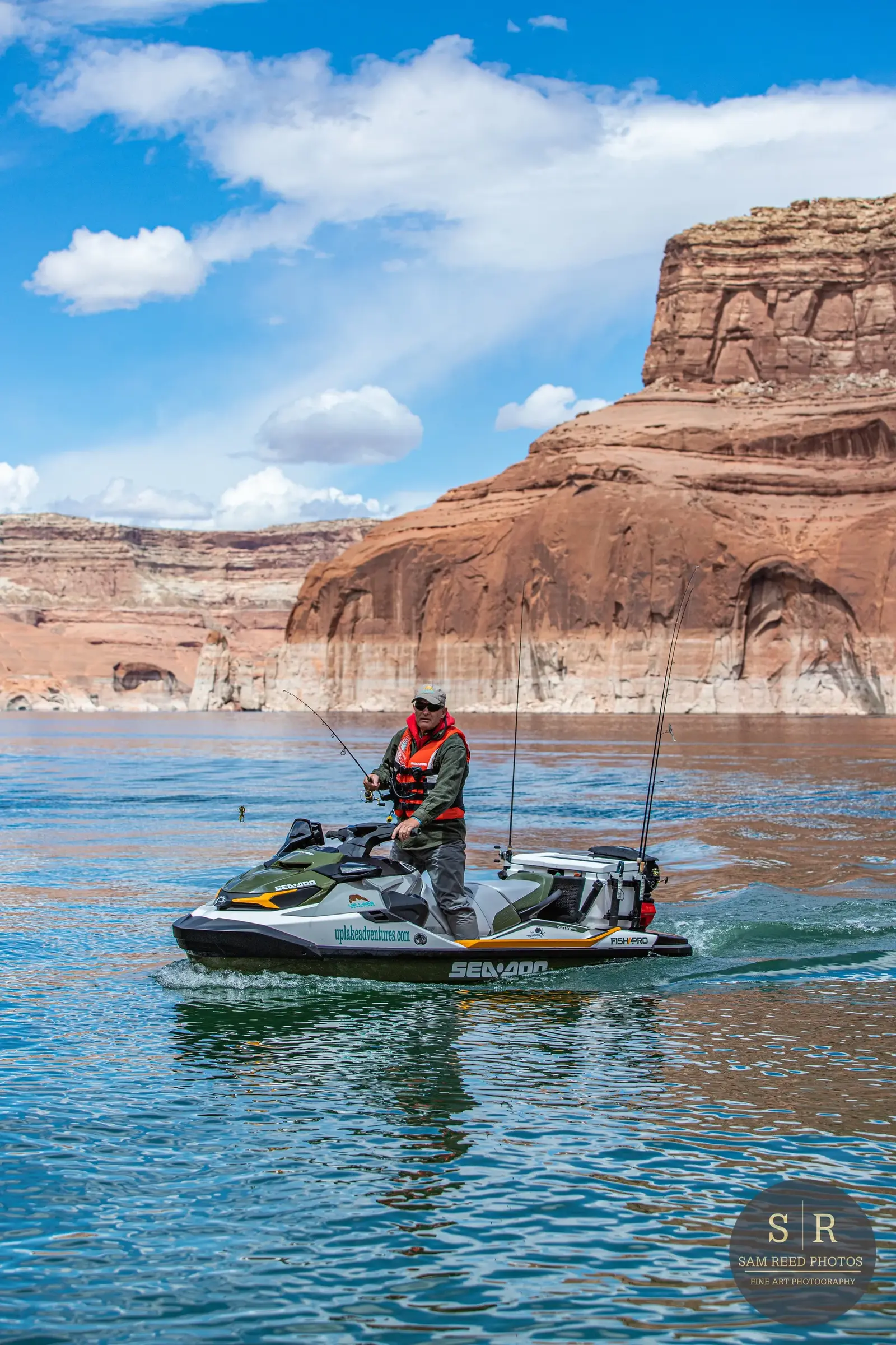 A man fishing on a sea-doo watercraft in a lake with red rock formations and blue sky in the background.