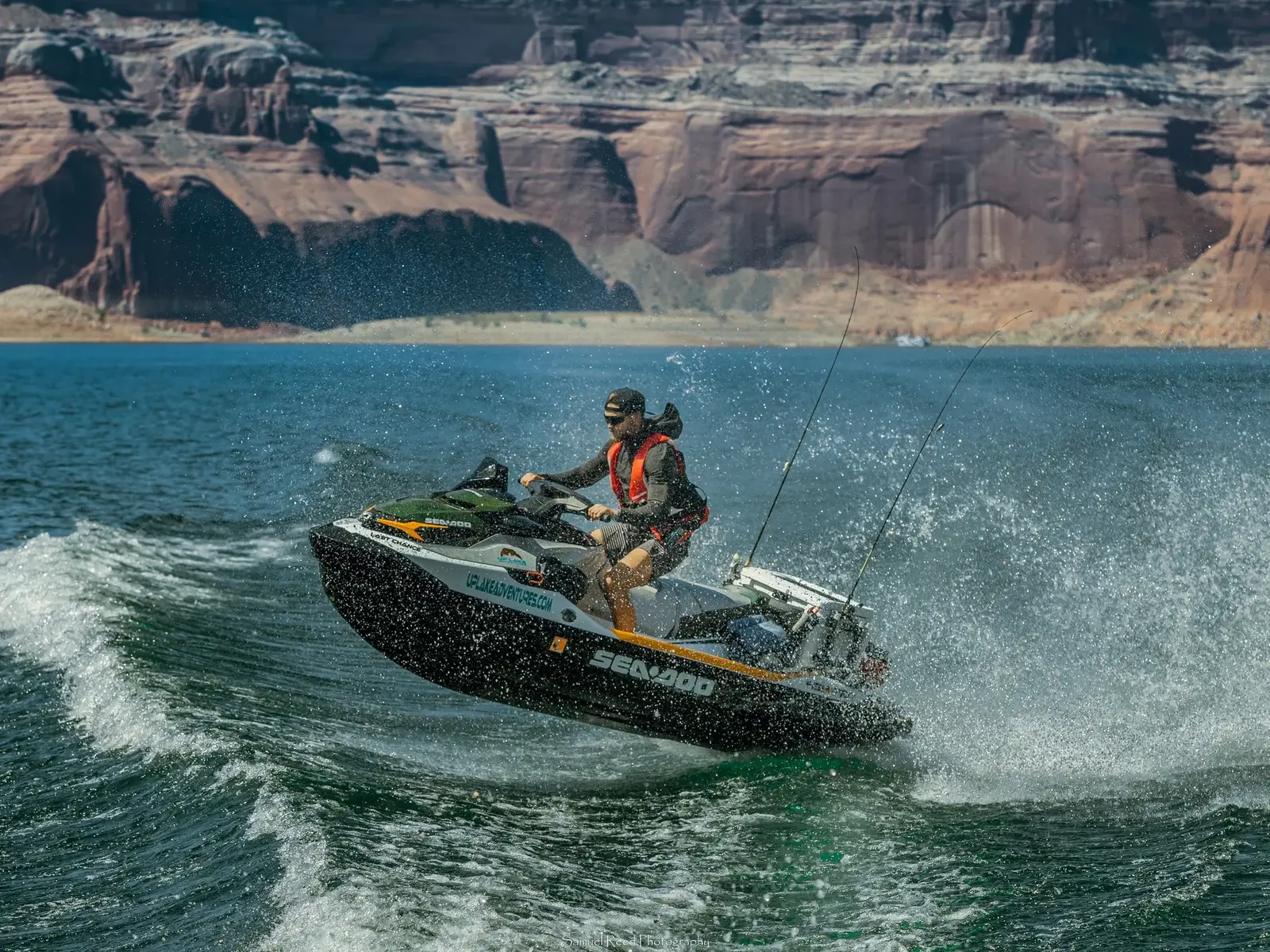 A person riding a black and green jet ski on a body of water with canyon walls in the background.