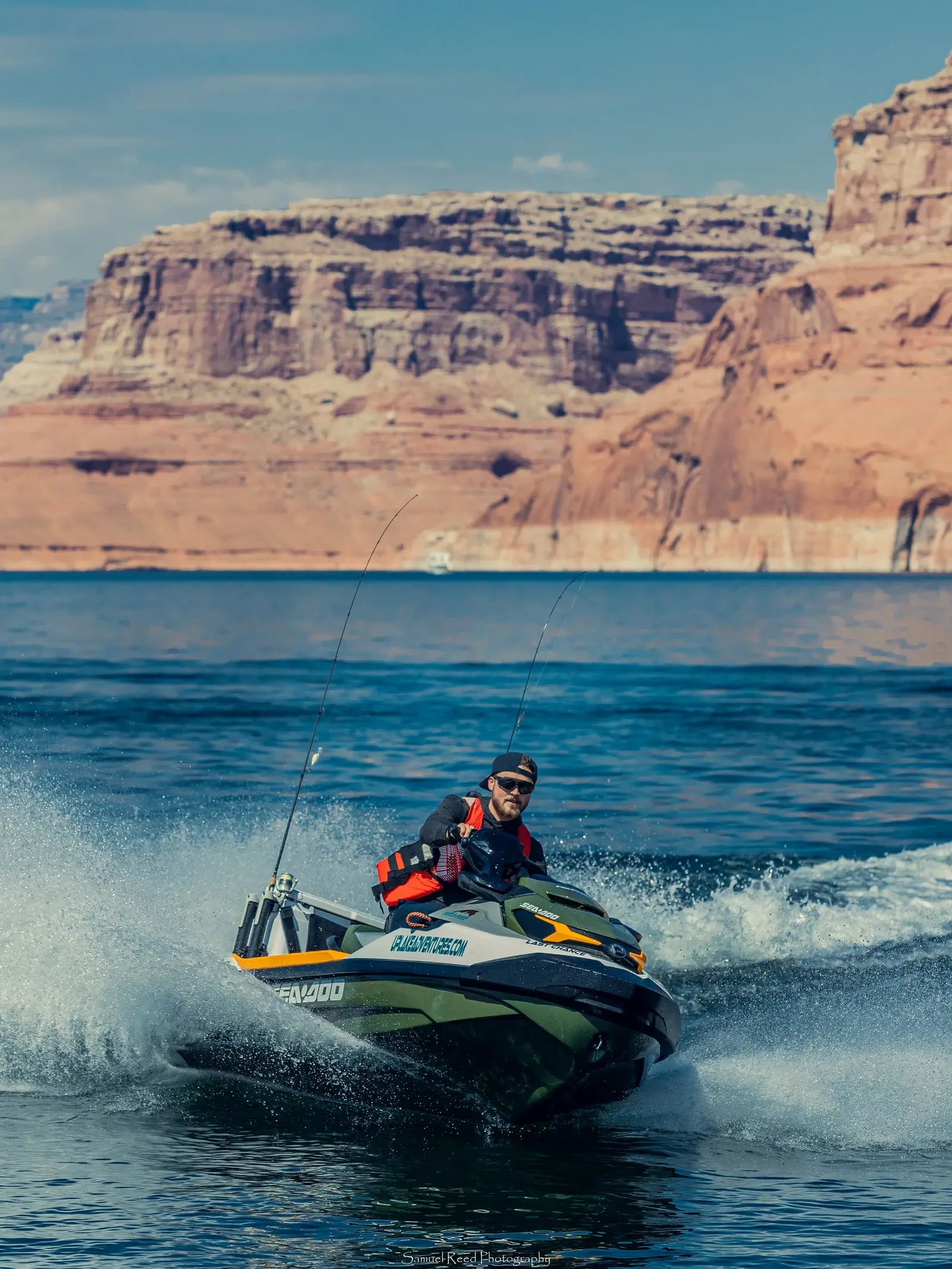 A man riding a jet ski on a large body of water with red rock canyon cliffs in the background.