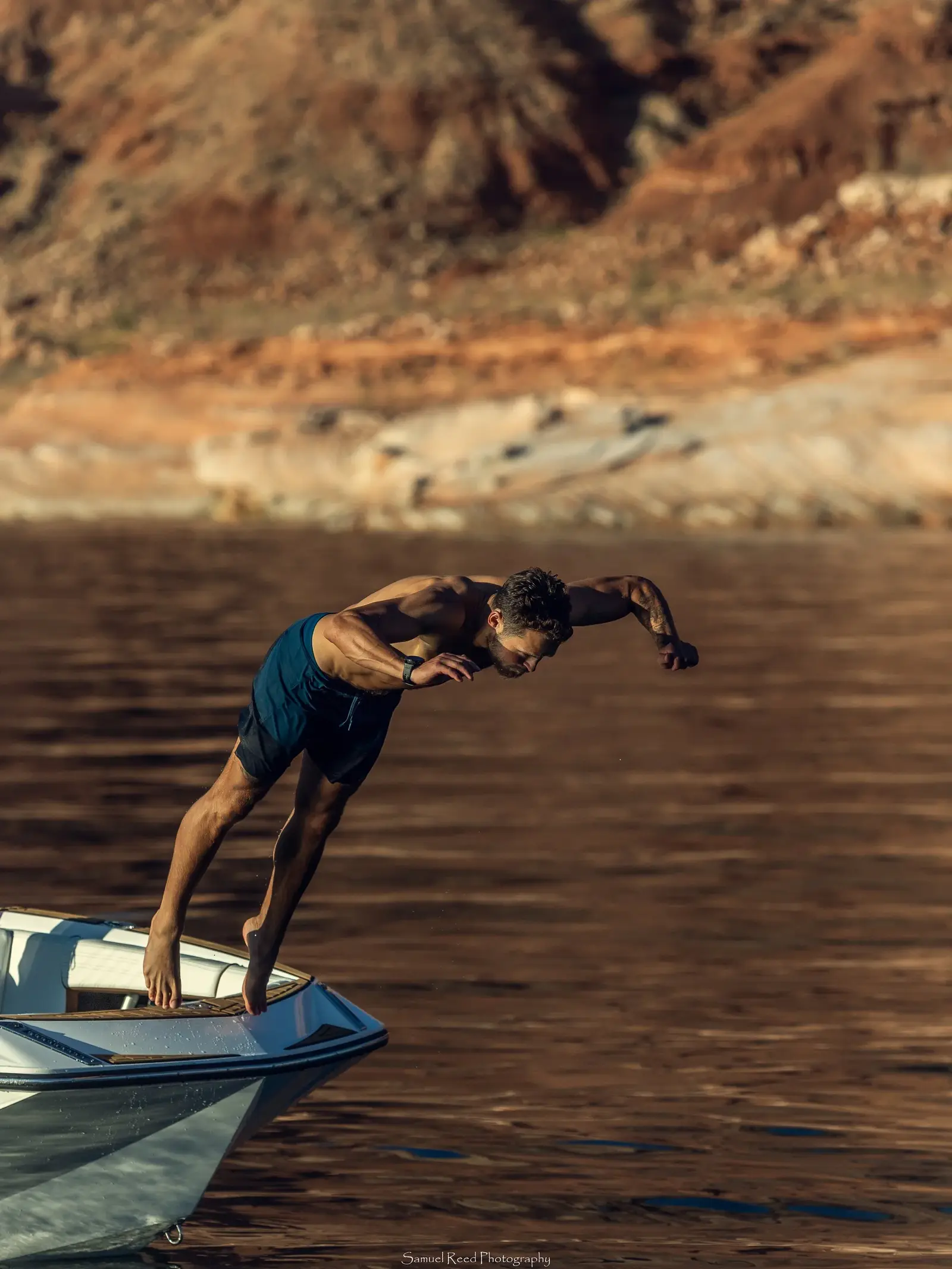 A man is diving off the edge of a boat into a body of water with rocky cliffs in the background.