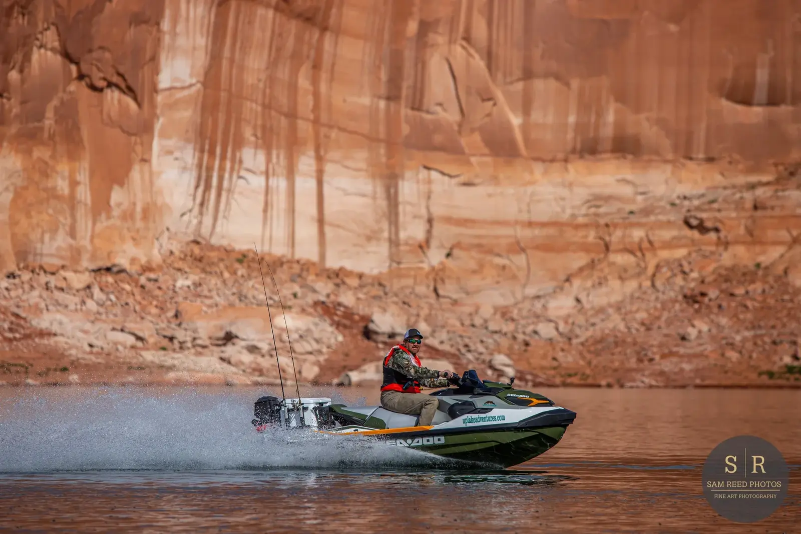 A man riding a jet ski on a body of water, with a rugged canyon wall in the background.