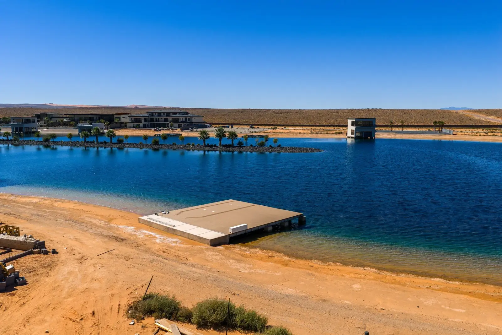 View over a sandy shoreline and dock toward water and buildings across the way.