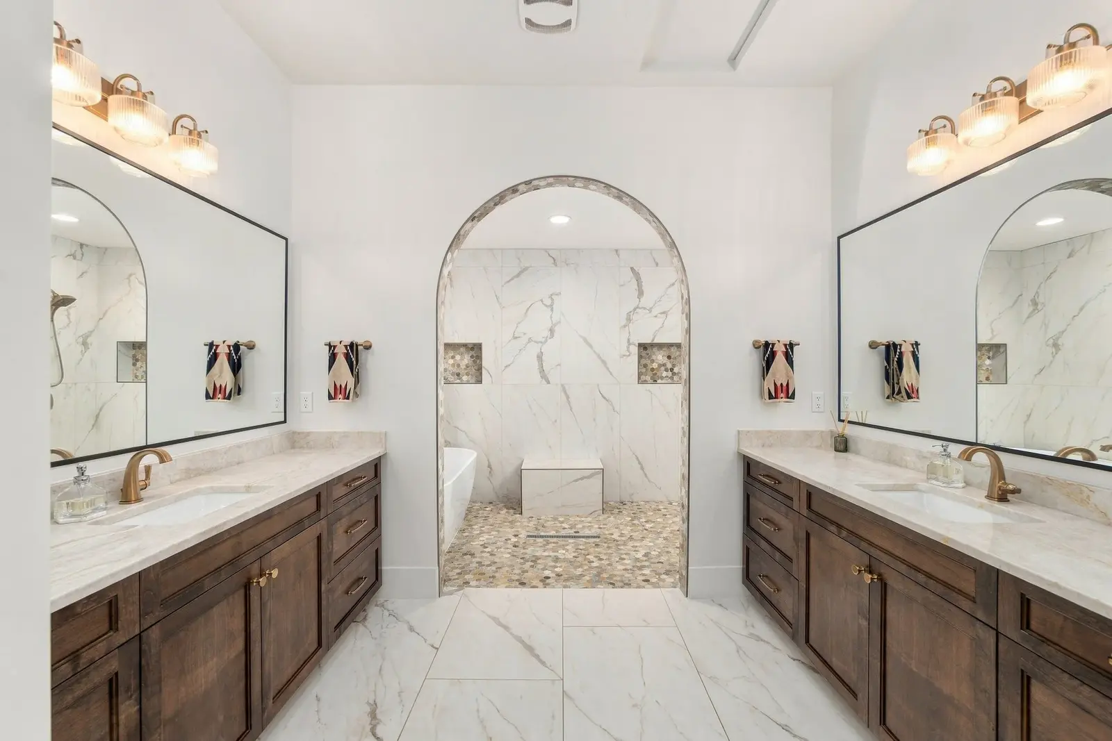 Bathroom with two wood vanities and an arched opening to a tiled shower area