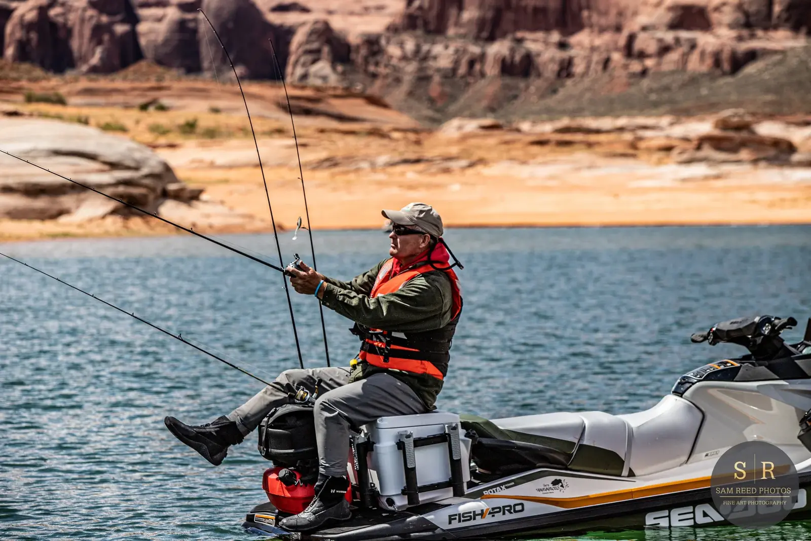 A man fishing from a watercraft on a large lake with rocky desert landscape in the background.