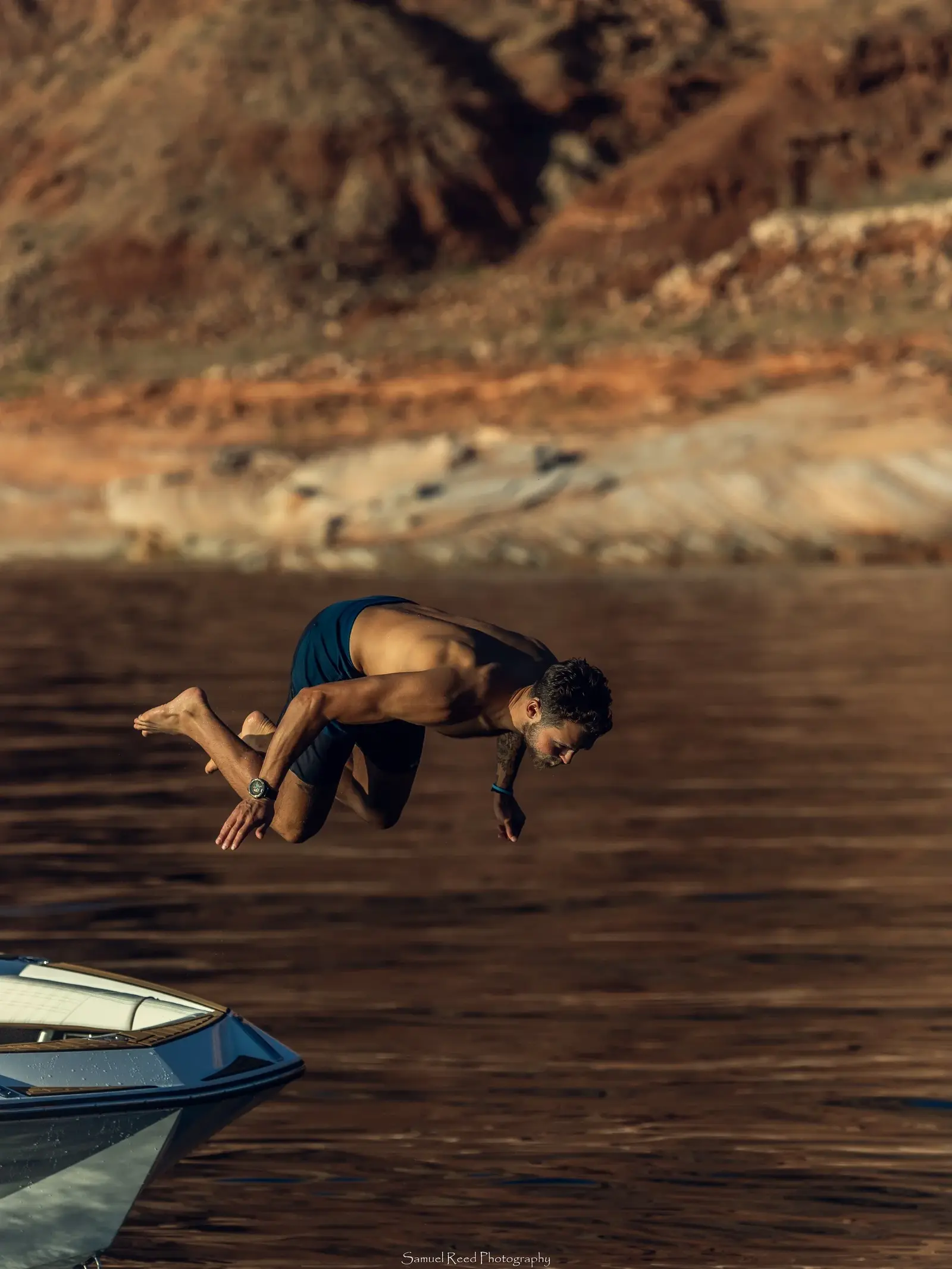 A man diving off a boat into a lake with a mountainous background.