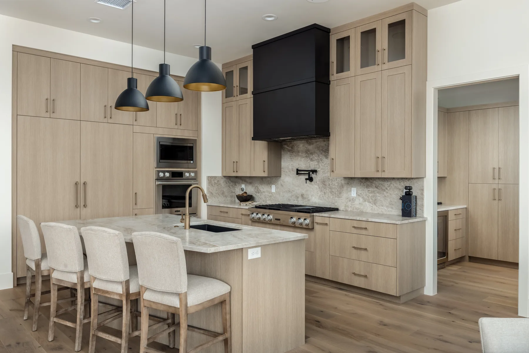 Light wood kitchen cabinetry, island seating, black pendant lights and a black range hood